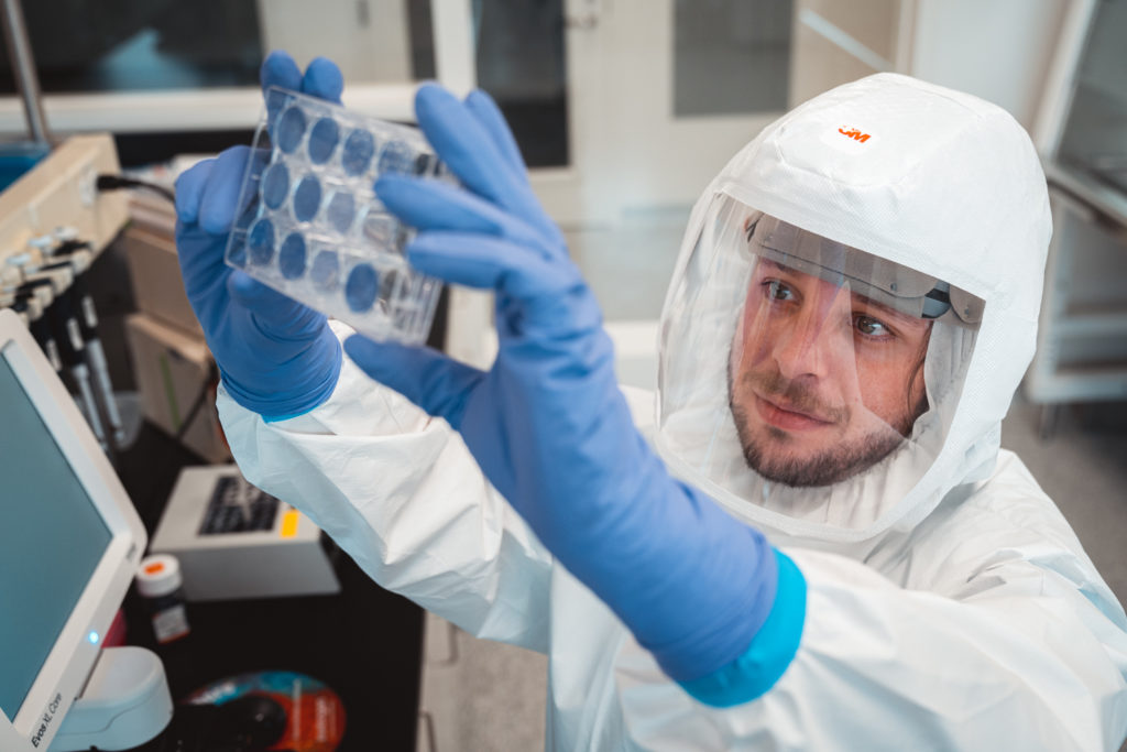 Man in cleanroom suit holding up samples