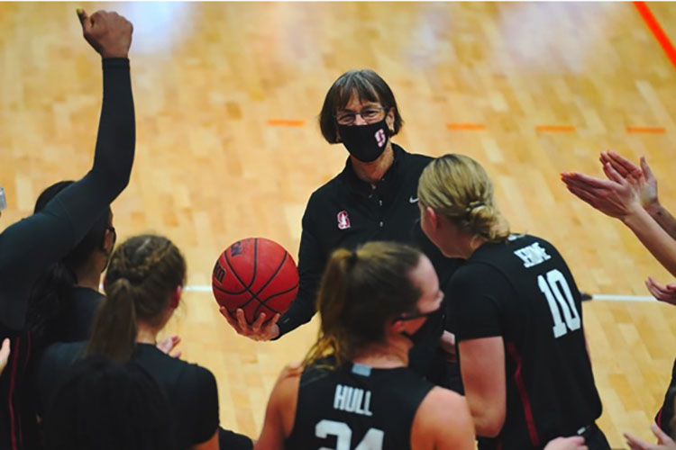 Tara VanDerveer holding a basketball with players around her.