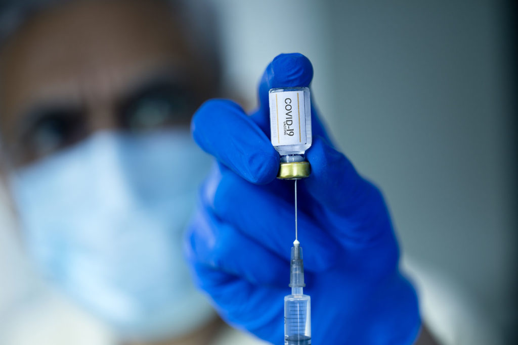 Doctor in surgical gloves pulling vaccine liquid from vial to vaccinate male patient