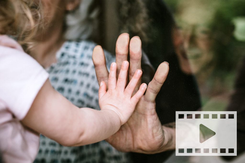 toddler and elder touch hands through glass