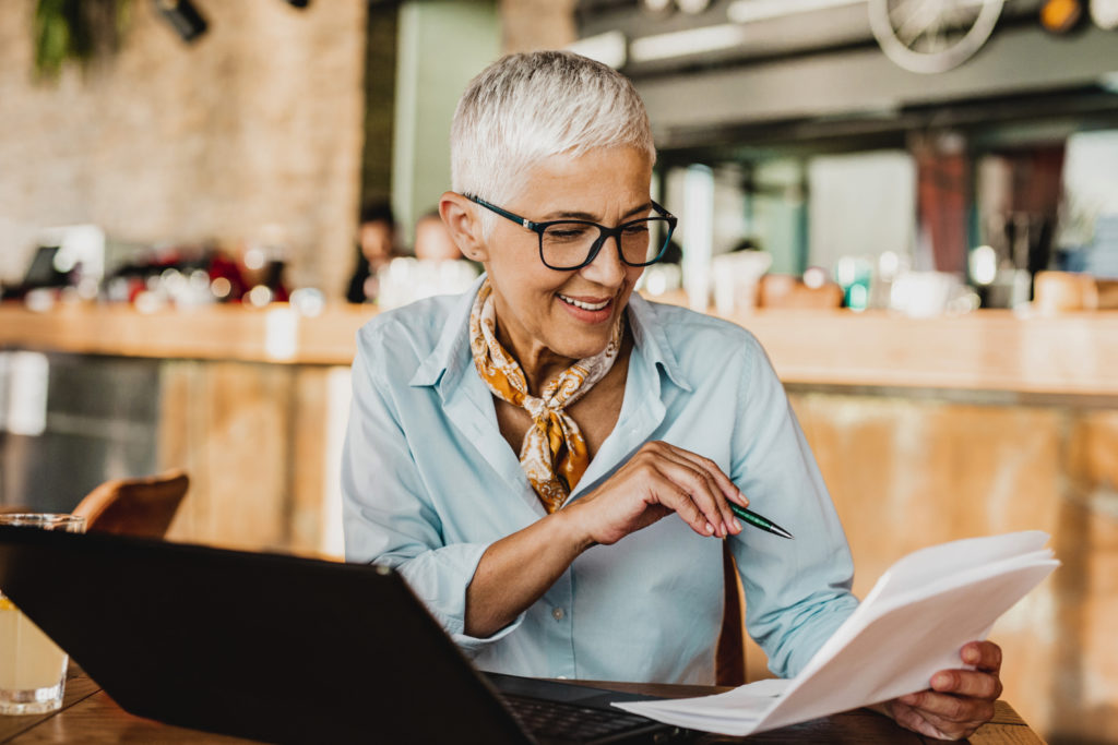 An older woman is sitting in a coffee shop and using laptop.