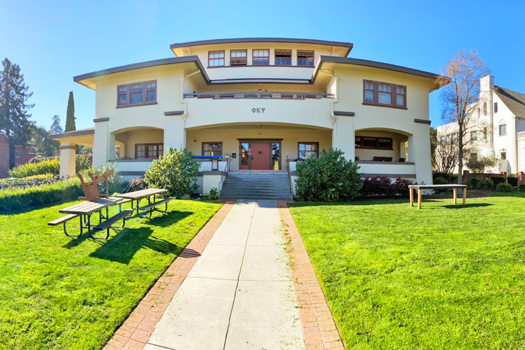 Exterior view of three-story house with lawn and picnic benches. Greek letters for Phi Kappa Psi are above the door.