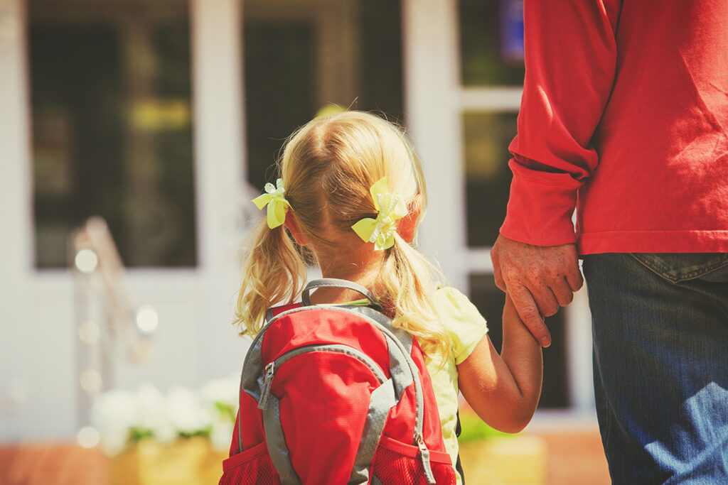 A father walking his young daughter to daycare.