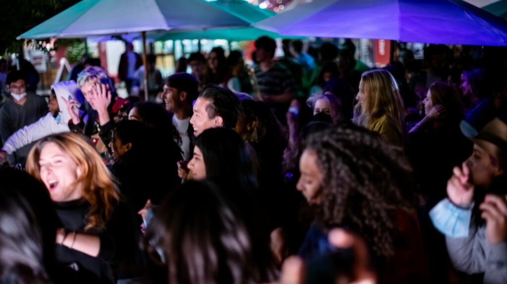 Student crowd facing stage, dancing, with stage lights shining on their faces.