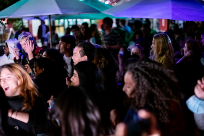 Student crowd facing stage, dancing, with stage lights shining on their faces.