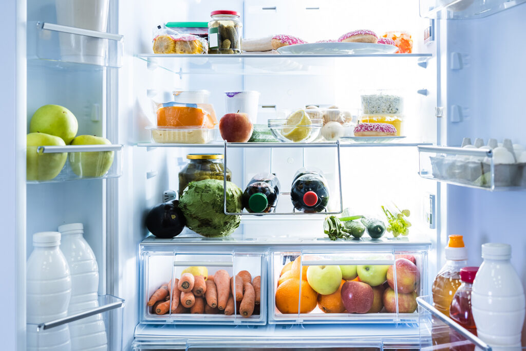 An open refrigerator that's clean and brightly lit, full of fruit, vegetables and junk food.