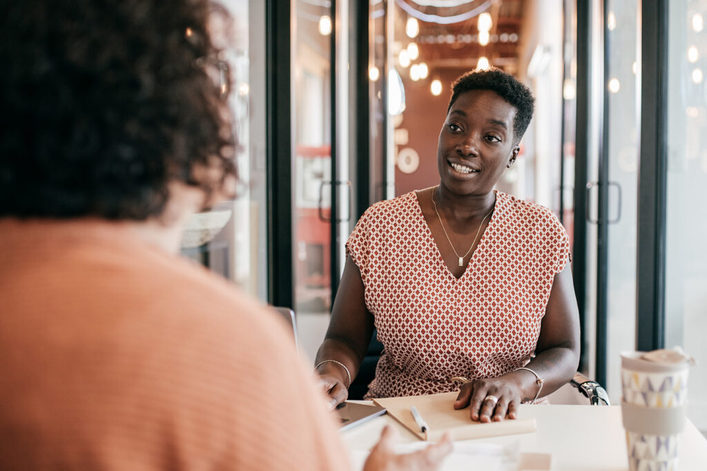 A Black woman sitting in an office with another female employee going over paperwork.