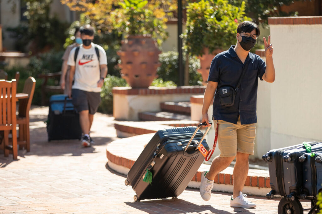 students walking away from dorm with suitcases