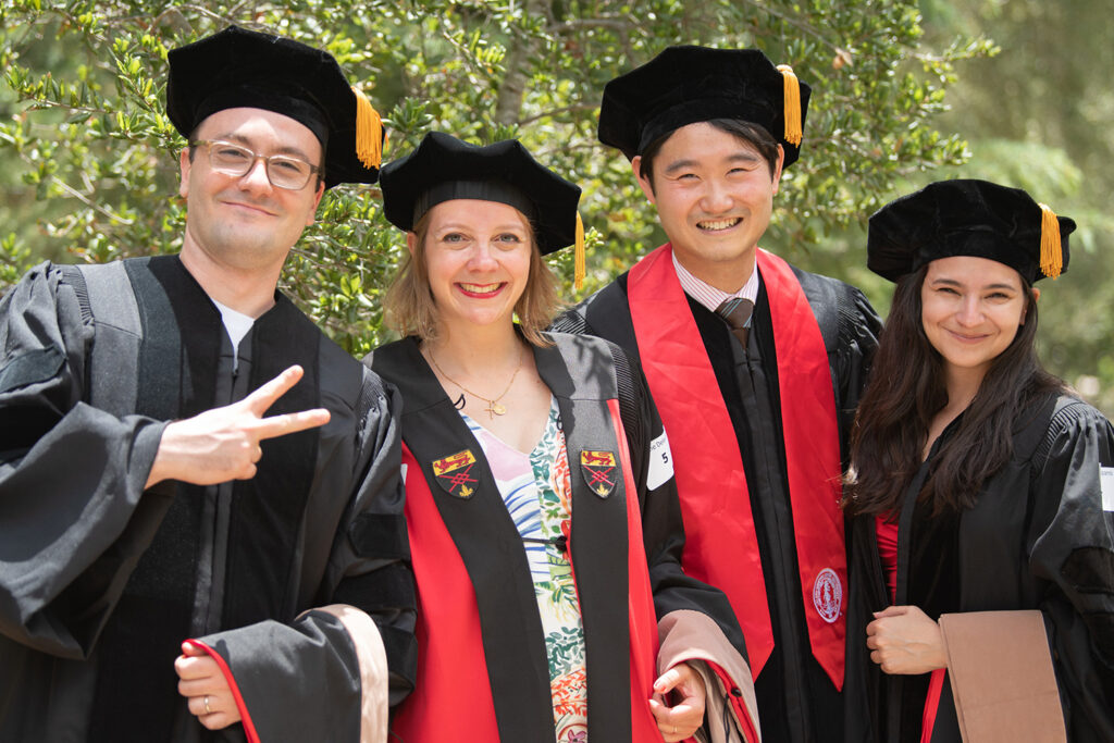 A group of four students in their cap and gowns smiling at the camera on graduation day.