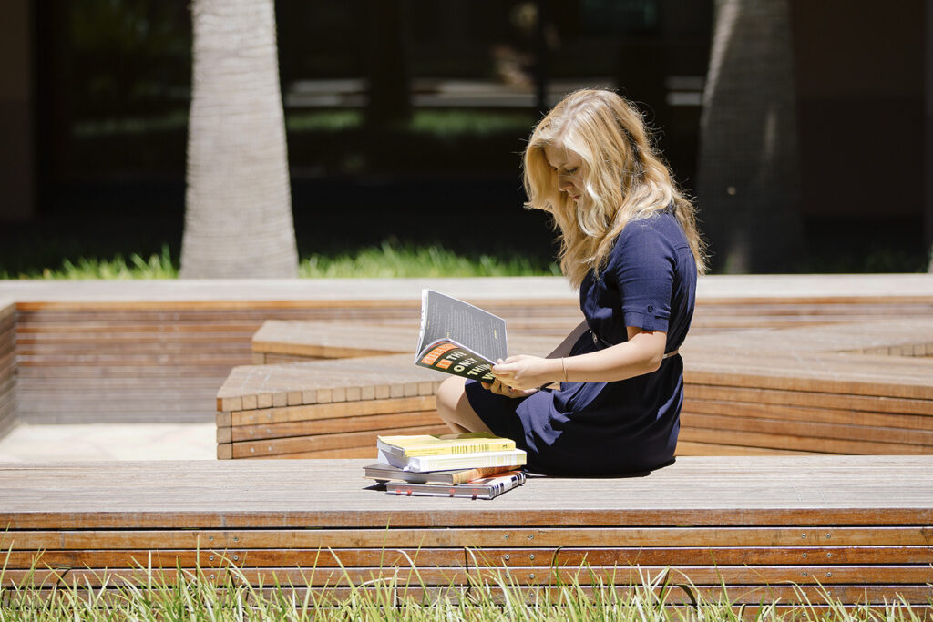 A student sits reading in McCoy Courtyard next to a stack of books.