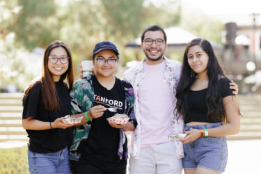 Four friends standing arm-in-arm, one wearing a Stanford t-shirt.