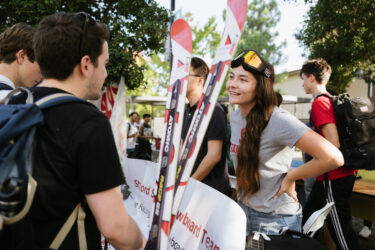 Student wearing ski goggles speaking to another student