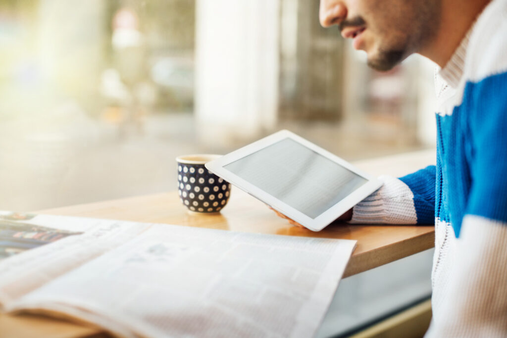 a man hunched over a table looking at a newspaper and an iPad.