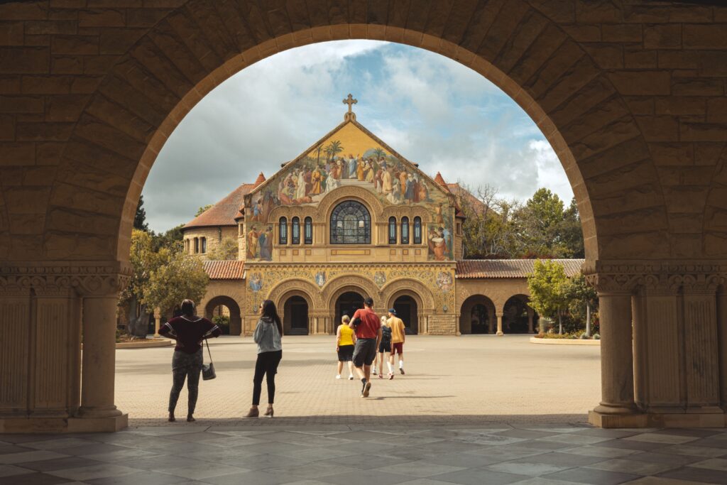 Memorial Church is seen through an arch, which is in shadow. People stroll in the foreground in the sun.