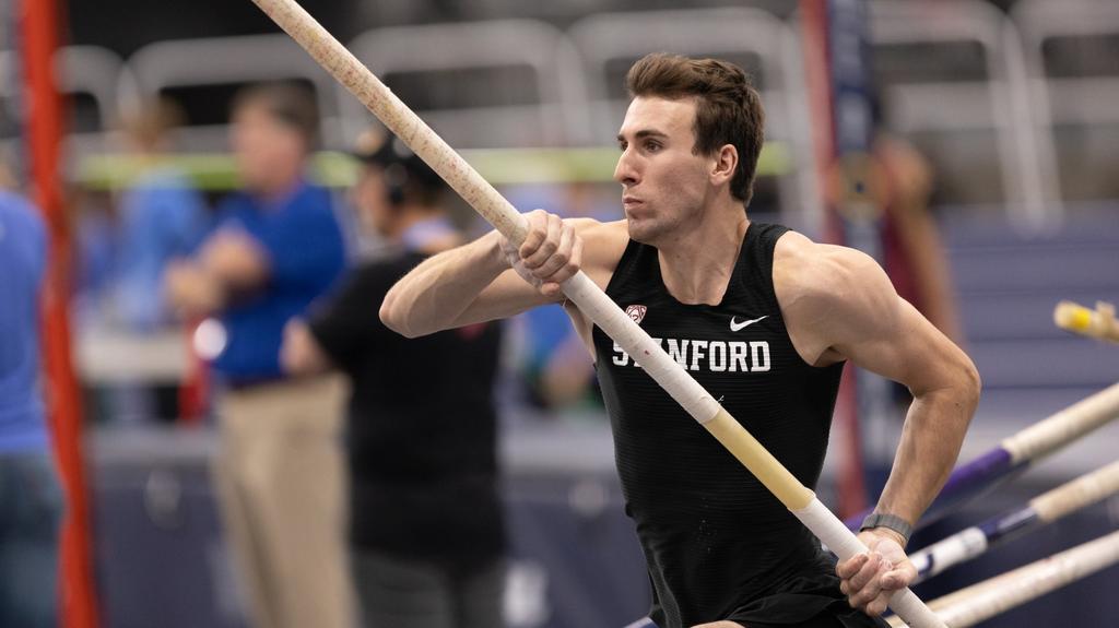 A young man wearing a black Stanford tank top prepares to pole vault.