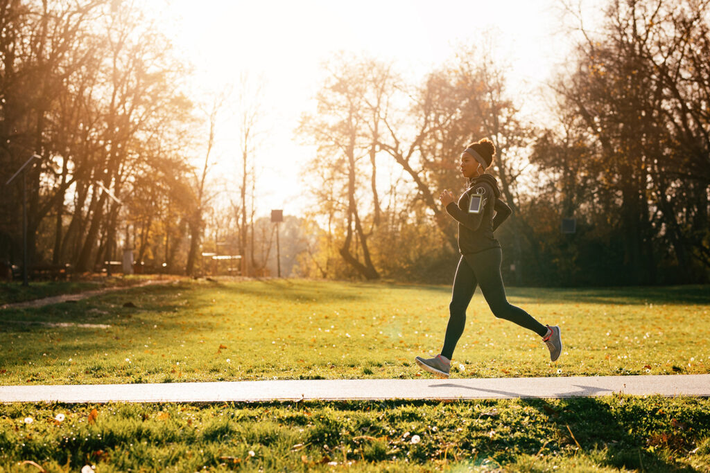 Woman jogging on a sunny path with grass behind her.