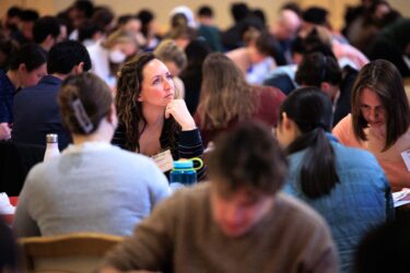 Image shows crowded meeting room and focuses on one conference participant looking up deep in thought while listening to a speaker.