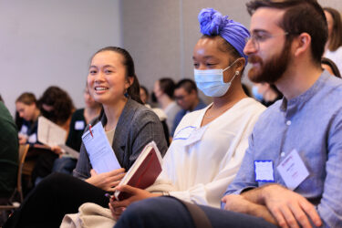 Image shows crowded meeting room and focuses on one conference participant looking up deep in thought while listening to a speaker.