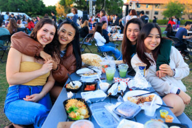 Four students seated at a picnic table, eating.