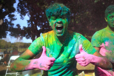 Student covered in colored dust, smiling.