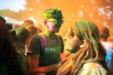 Student covered in colored dust, smiling.