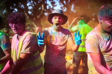 Student covered in colored dust, smiling.