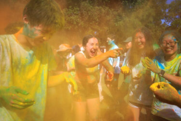 Student covered in colored dust, smiling.