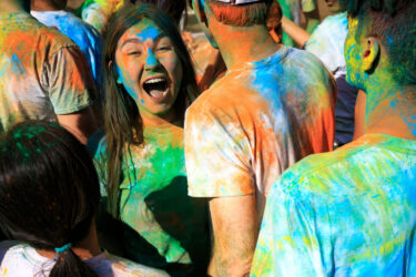 Student covered in colored dust, smiling.