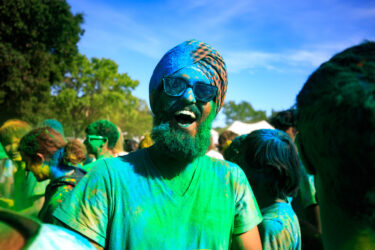 Student covered in colored dust, smiling.