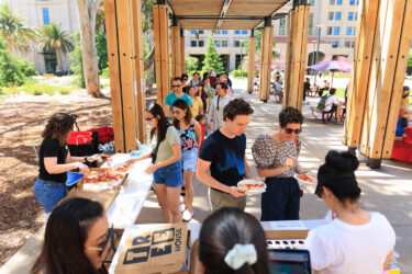 Students under an outdoor arbor, picking up lunch.