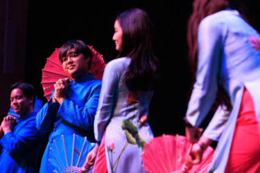 Student performing a dance, carrying red umbrellas.