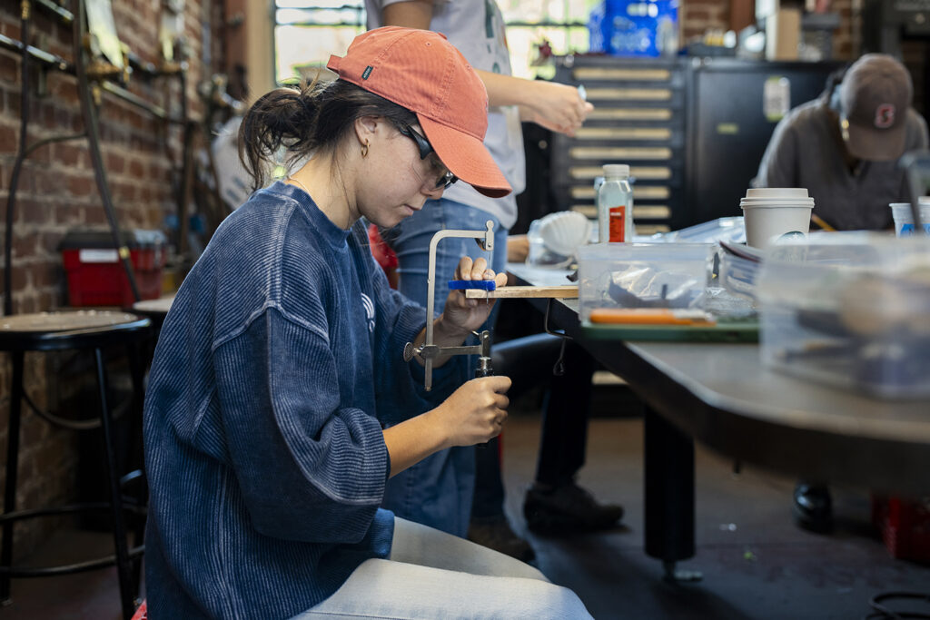 Undergraduate student Symphony Koss uses a coping saw to works on her project.