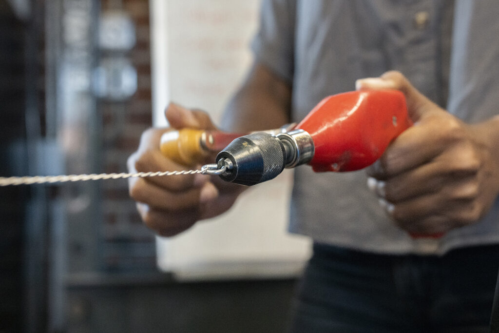 Student uses a hand drill to twist wire.