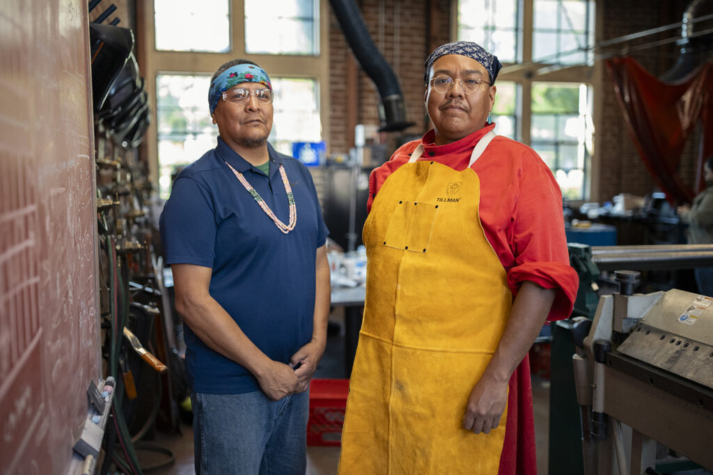 Navajo artists Robert Blackhat Jr. and Zefren Anderson pose for a portrait in the workshop.