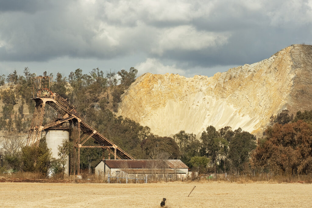 Landscape of old disused mineshaft, showing a mine dump behind, and heavy rain clouds, in Boksburg South Africa