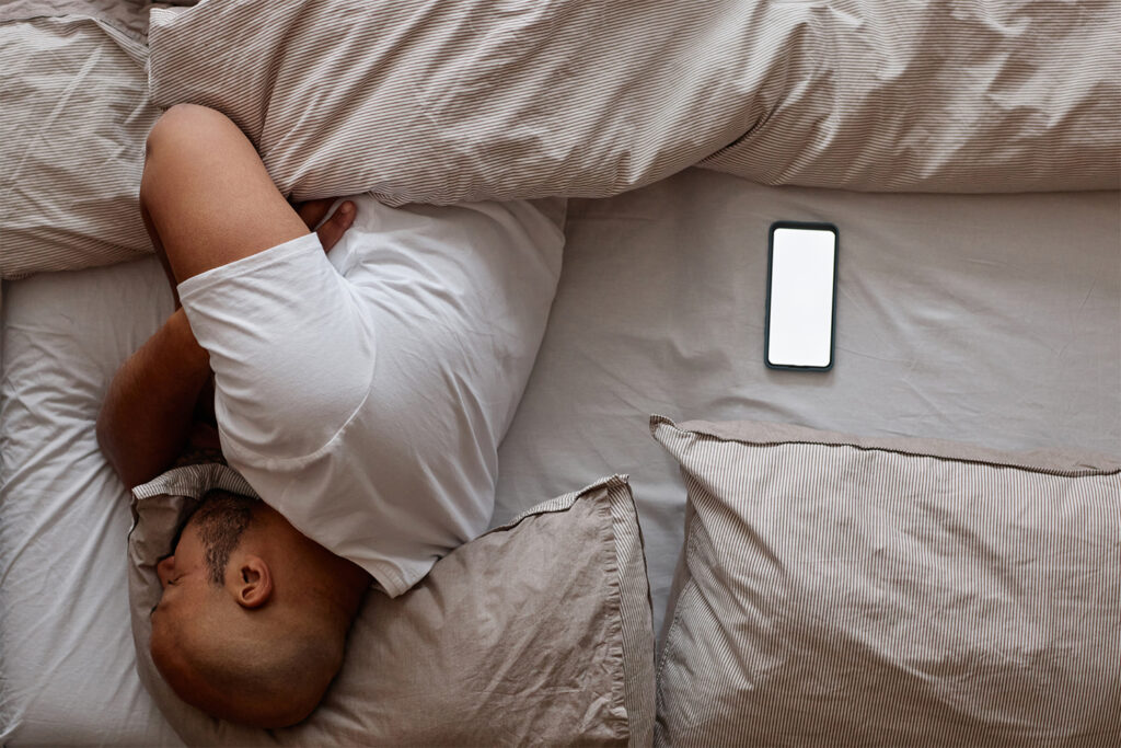 Man in bed asleep, phone next to him with a blank screen