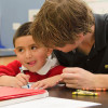 Young man helping a small boy with his school work. / Photo: Joy Leighton