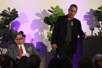 Russ Altman seated and Yoav Shoham standing in front of an audience.