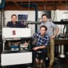 Three men posing in a lab with a machine