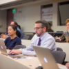 People in a tiered classroom, many with laptop computers