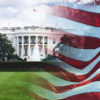 A front-lawn view of the white house, with an american flag flying on the foreground