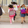 Young elementary school kids running up steps to school, back view