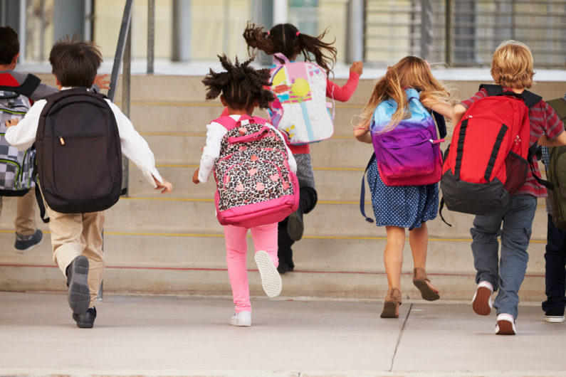 Young elementary school kids running up steps to school, back view