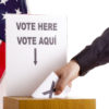 Hand inserting a ballot to voting box. The sign above the slot in two languages, English and Spanish. USA flag and white background.