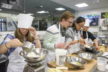 members of class in kitchen measuring ingredients