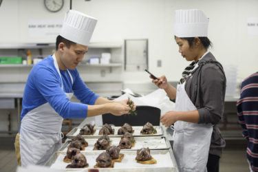 student garnishing wood pigeon while classmate takes photo