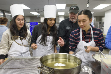 students and chef at the stove heating a pan of oil