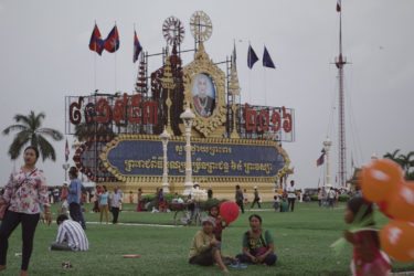 many people on a lawn, with an orate sign behind them