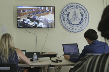 people working on laptops as they observe a televised trial