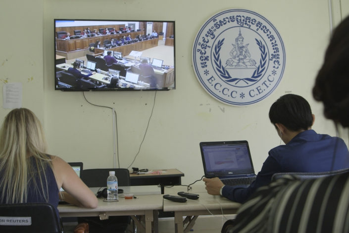 people working on laptops as they observe a televised trial)